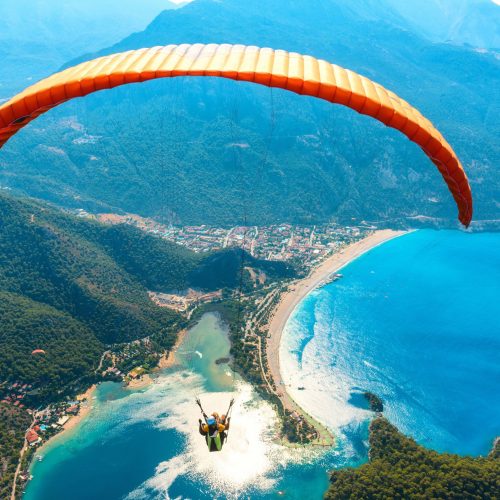 Paragliding in the sky. Paraglider tandem flying over the sea with blue water and mountains in bright sunny day. Aerial view of paraglider and Blue Lagoon in Oludeniz, Turkey. Extreme sport. Landscape